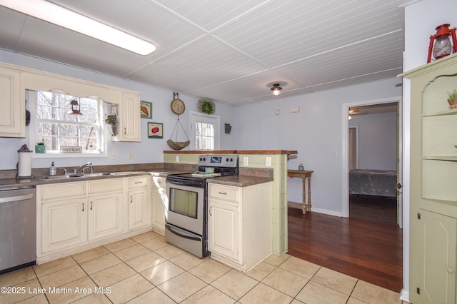 kitchen featuring sink, light tile patterned floors, stainless steel appliances, kitchen peninsula, and cream cabinetry