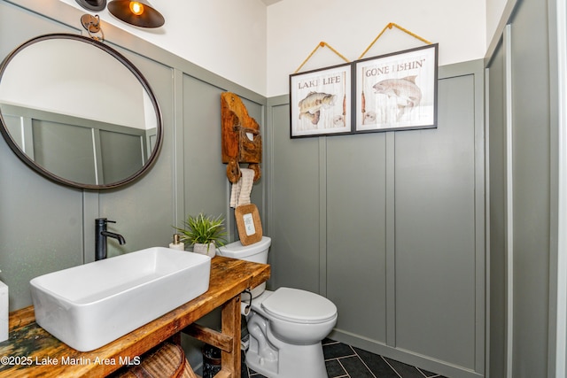 bathroom with a sink, toilet, tile patterned floors, and a decorative wall