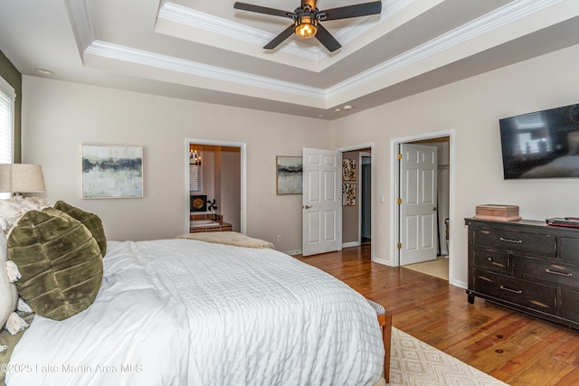 bedroom with ornamental molding, a raised ceiling, baseboards, and wood finished floors