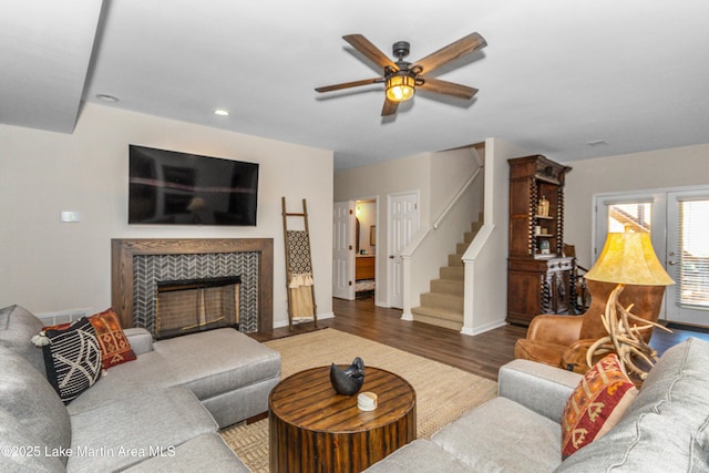 living room featuring ceiling fan, baseboards, stairs, a fireplace, and wood finished floors