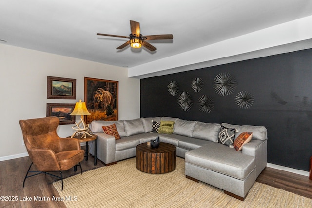 living room featuring ceiling fan, baseboards, wood finished floors, and an accent wall