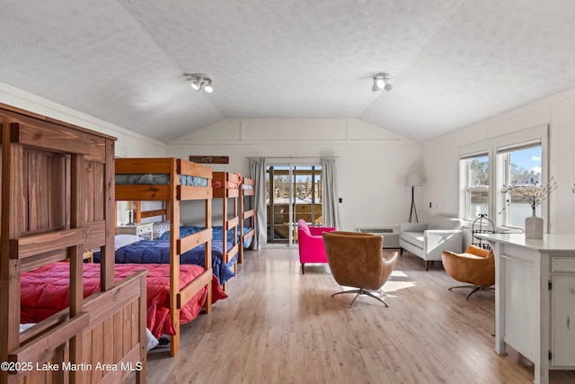 bedroom featuring a textured ceiling, light wood-style flooring, and vaulted ceiling