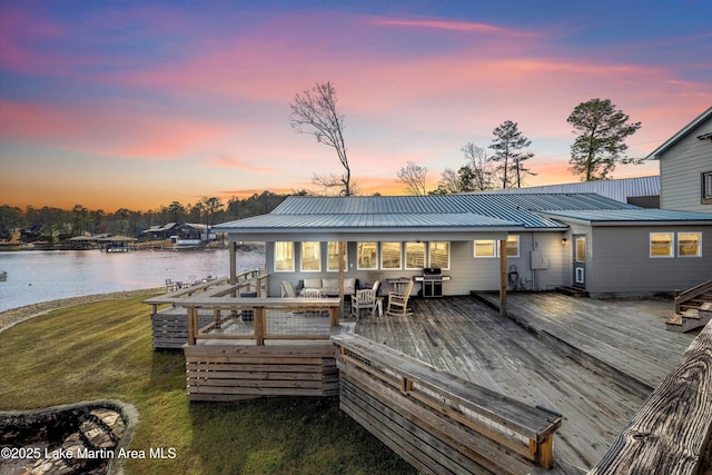 exterior space featuring metal roof, a deck with water view, and a yard