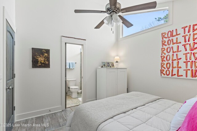 bedroom with connected bathroom, ceiling fan, baseboards, a towering ceiling, and wood finished floors