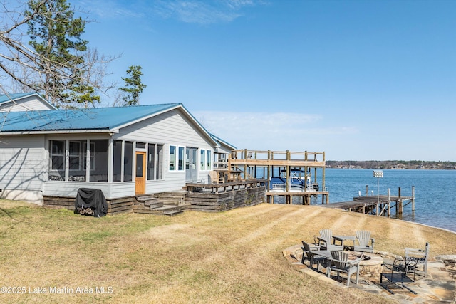 view of dock featuring a fire pit, a water view, and a lawn