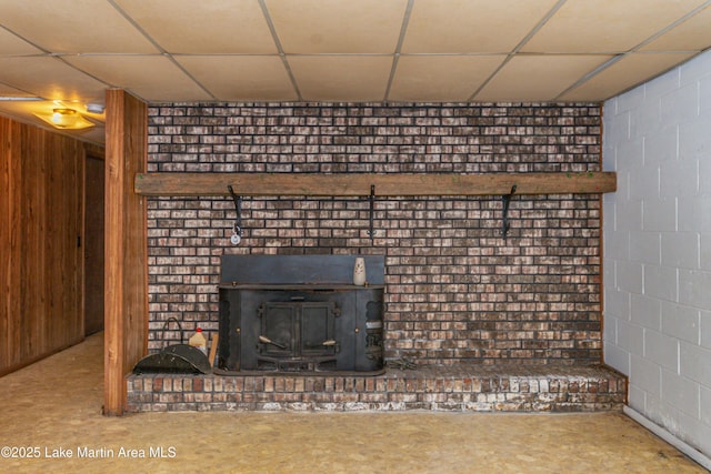 interior details with a paneled ceiling, concrete flooring, and a wood stove