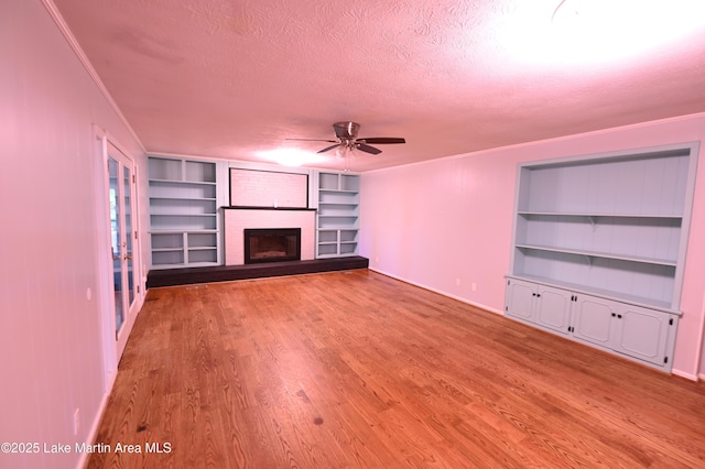 unfurnished living room featuring a textured ceiling, ceiling fan, wood finished floors, and built in shelves