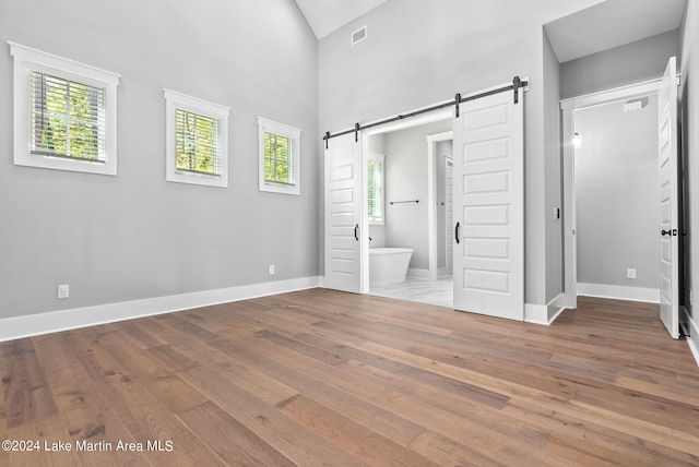 unfurnished bedroom featuring a barn door, light hardwood / wood-style flooring, multiple windows, and connected bathroom