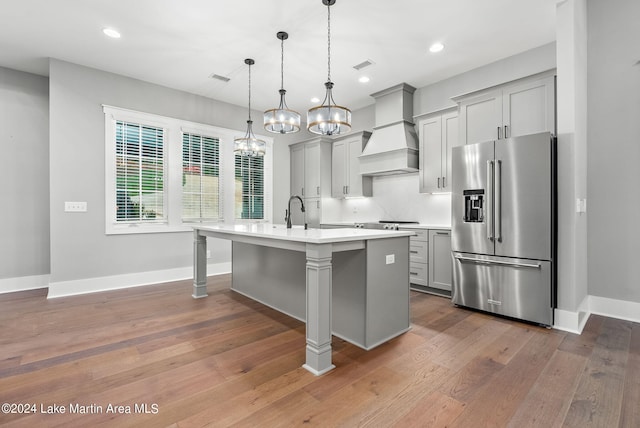 kitchen with custom range hood, stainless steel appliances, a kitchen island with sink, hardwood / wood-style floors, and gray cabinets