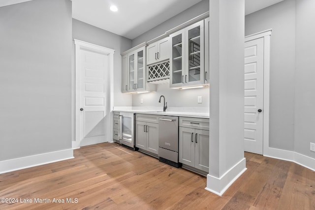 bar featuring sink, light hardwood / wood-style flooring, stainless steel dishwasher, gray cabinets, and beverage cooler