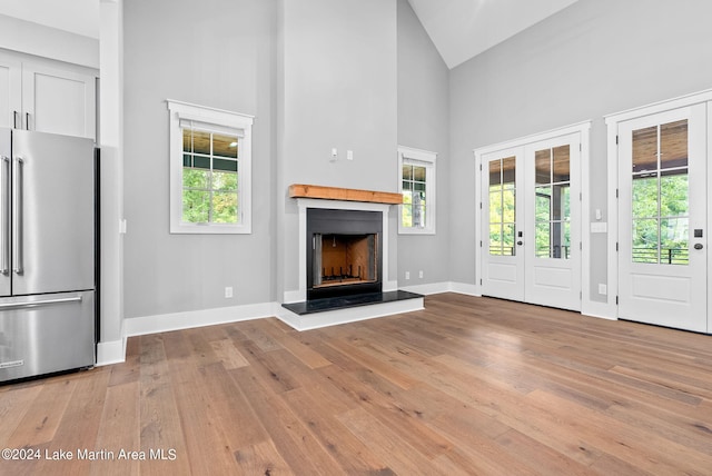 unfurnished living room with french doors, high vaulted ceiling, and light hardwood / wood-style floors