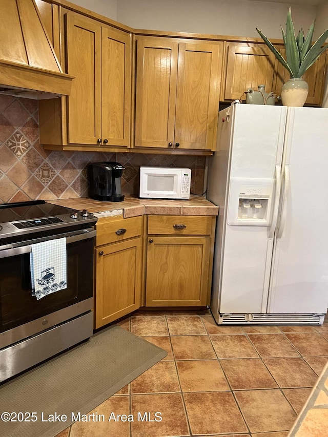 kitchen featuring light tile patterned flooring, custom range hood, white appliances, and decorative backsplash