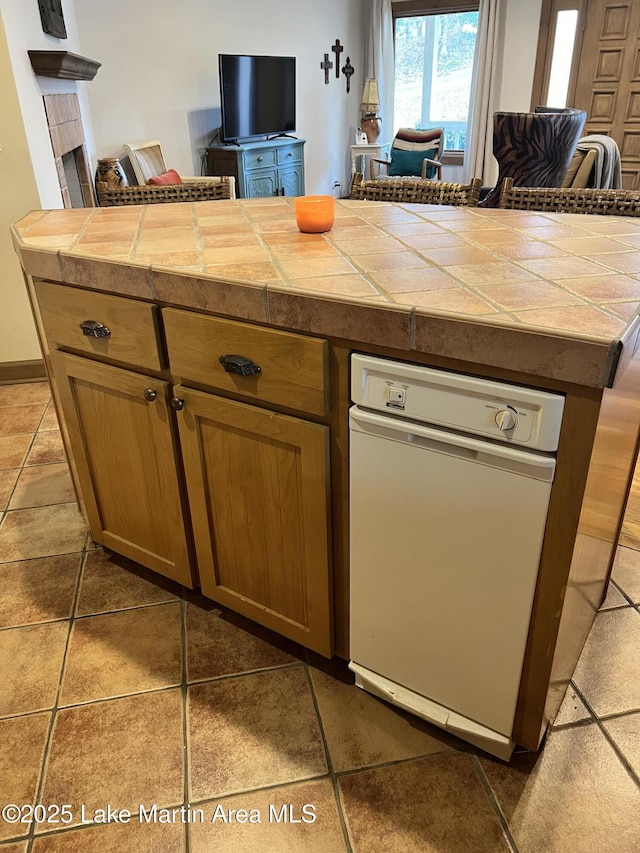 kitchen featuring tile countertops, dishwasher, a tile fireplace, and dark tile patterned floors