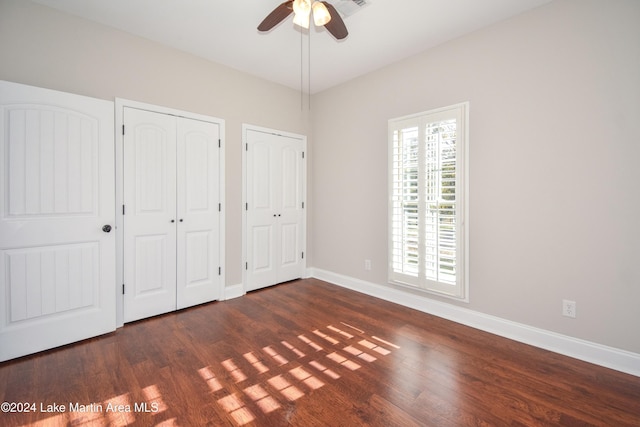 unfurnished bedroom featuring two closets, dark hardwood / wood-style floors, and ceiling fan