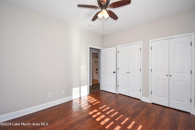 unfurnished bedroom featuring ceiling fan, dark hardwood / wood-style flooring, and multiple closets