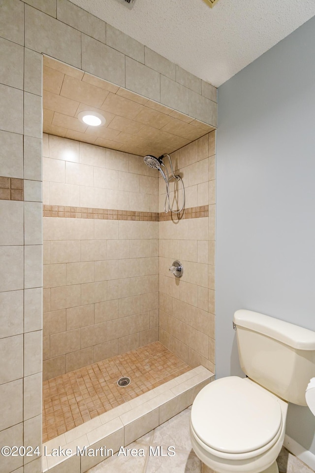 bathroom with tiled shower, toilet, and a textured ceiling