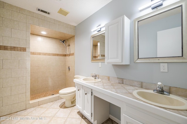 bathroom with vanity, tile patterned floors, toilet, and tiled shower