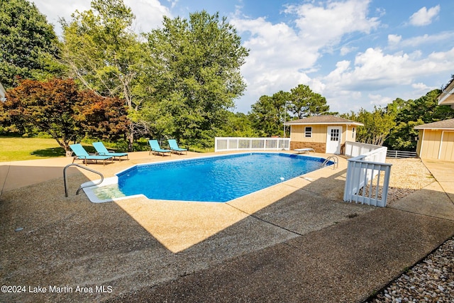 view of swimming pool with an outdoor structure, a diving board, and a patio