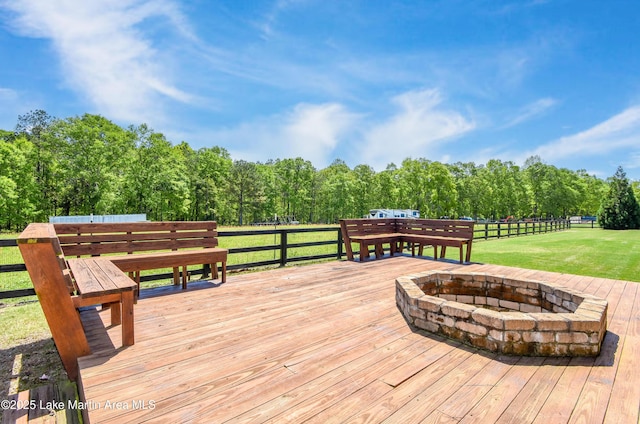 wooden terrace featuring a view of trees, fence, a fire pit, and a lawn