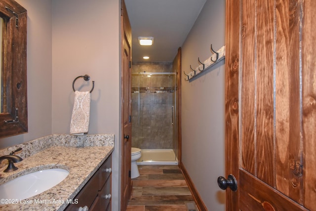 bathroom with toilet, a stall shower, wood finished floors, and vanity