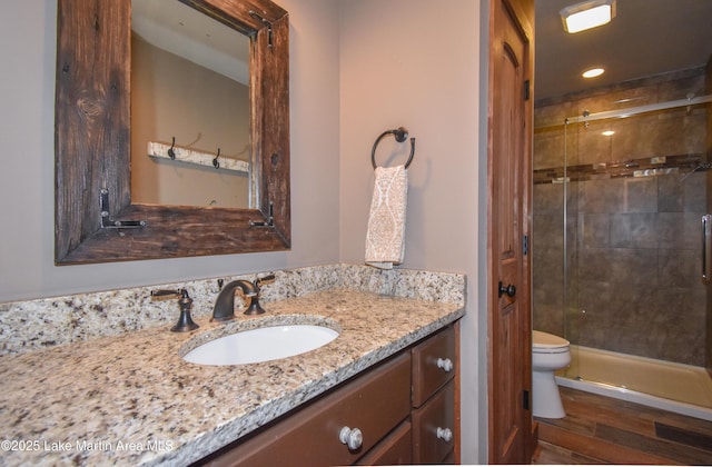 full bath featuring a shower stall, wood finished floors, vanity, and toilet