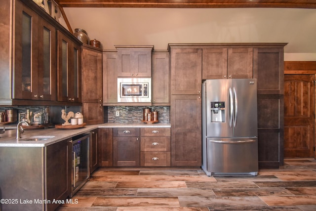kitchen featuring tasteful backsplash, stainless steel refrigerator with ice dispenser, wood finished floors, a sink, and wine cooler