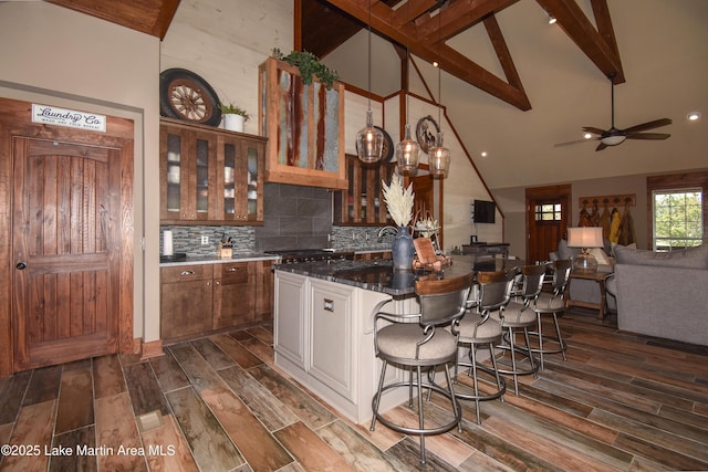 kitchen featuring tasteful backsplash, glass insert cabinets, a kitchen bar, beam ceiling, and dark wood finished floors