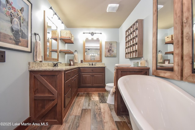 bathroom with a freestanding tub, a sink, toilet, double vanity, and wood finished floors