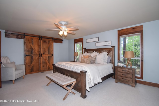 bedroom with ceiling fan, multiple windows, a barn door, and light carpet