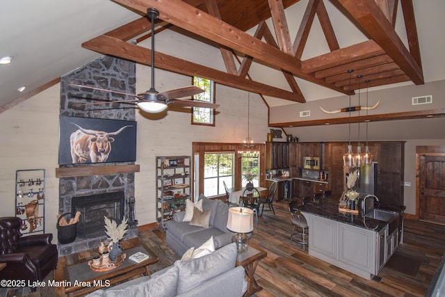 living room with visible vents, a stone fireplace, ceiling fan with notable chandelier, dark wood-type flooring, and high vaulted ceiling