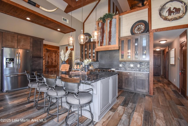 kitchen featuring lofted ceiling with beams, glass insert cabinets, a kitchen bar, stainless steel fridge, and backsplash