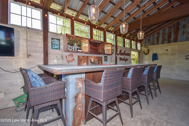 bar with pendant lighting, high vaulted ceiling, wood walls, and indoor bar