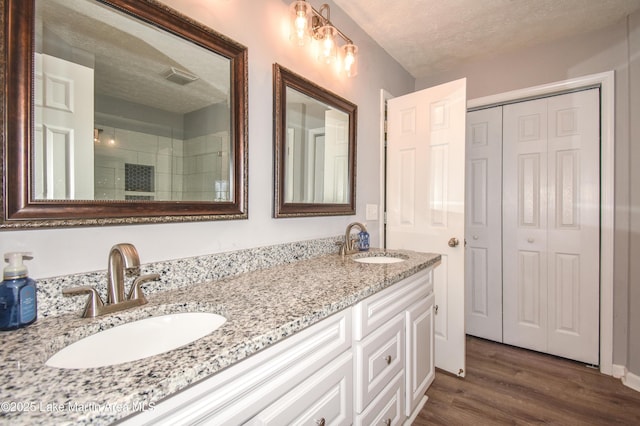 bathroom with a tile shower, a sink, a textured ceiling, and wood finished floors