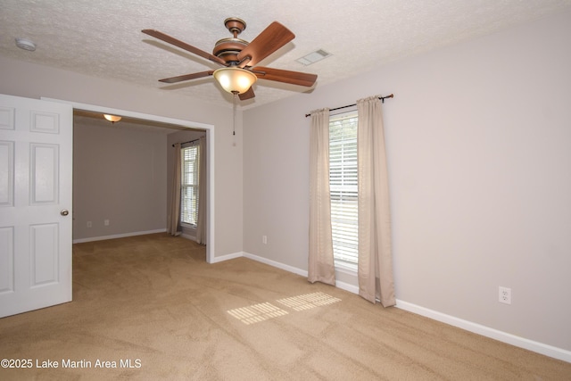 carpeted empty room with a ceiling fan, visible vents, a textured ceiling, and baseboards