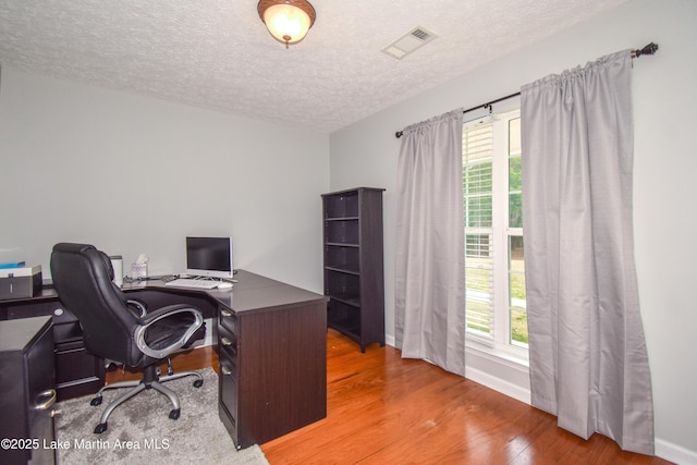 office area featuring a textured ceiling, plenty of natural light, wood finished floors, and visible vents