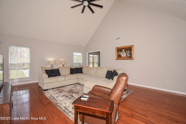 living room with ceiling fan, high vaulted ceiling, wood finished floors, visible vents, and baseboards