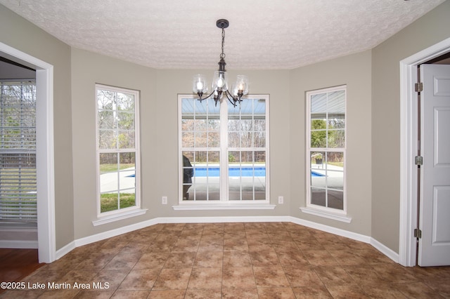 unfurnished dining area featuring a textured ceiling, baseboards, and a notable chandelier