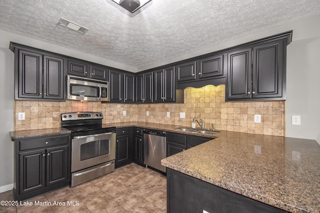 kitchen with appliances with stainless steel finishes, visible vents, a sink, and dark cabinetry