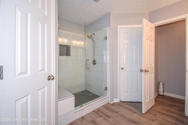 full bathroom with a stall shower, a textured ceiling, baseboards, and wood finished floors