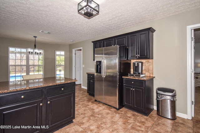 kitchen featuring dark stone countertops, stainless steel refrigerator with ice dispenser, and dark cabinetry