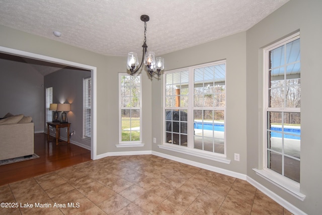 unfurnished dining area featuring baseboards, a textured ceiling, tile patterned floors, and an inviting chandelier