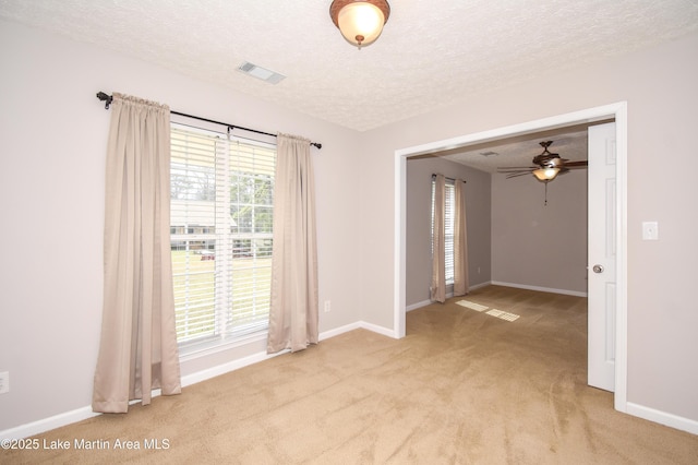 empty room with light carpet, a textured ceiling, visible vents, and baseboards