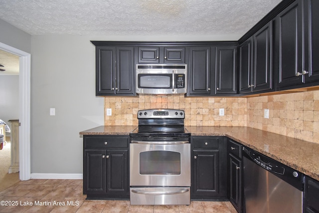 kitchen with appliances with stainless steel finishes, backsplash, dark cabinetry, and dark stone counters