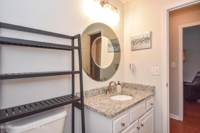 half bath featuring toilet, baseboards, wood finished floors, and vanity