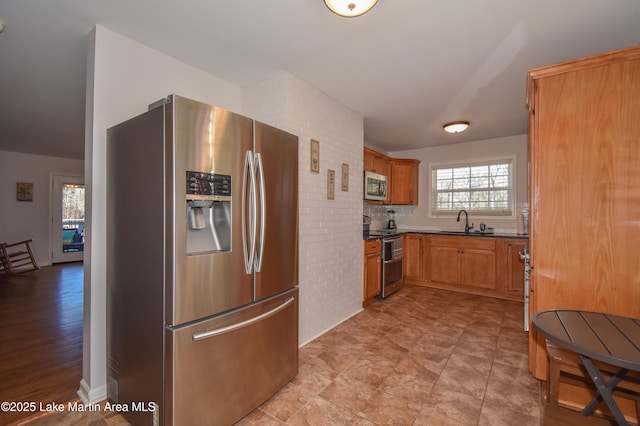 kitchen featuring sink, backsplash, appliances with stainless steel finishes, and brick wall