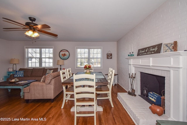 dining space with a fireplace, brick wall, dark wood-type flooring, and ceiling fan