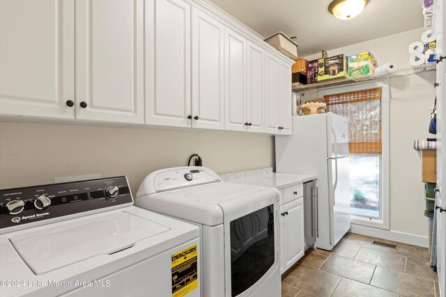 clothes washing area featuring separate washer and dryer, light tile patterned floors, and cabinets