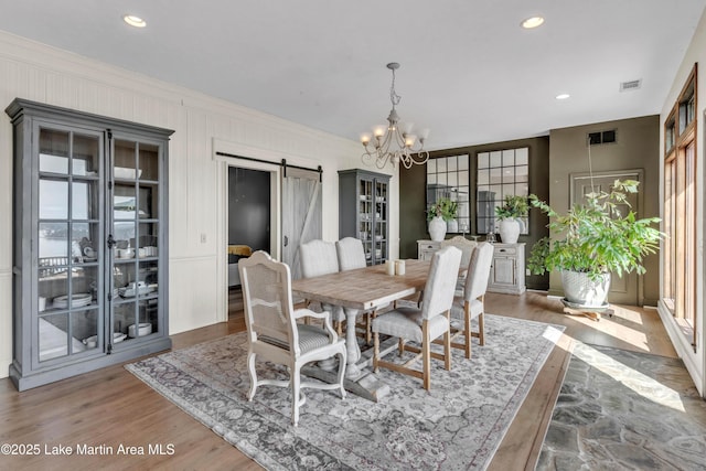 dining room featuring hardwood / wood-style floors, ornamental molding, a barn door, and a chandelier