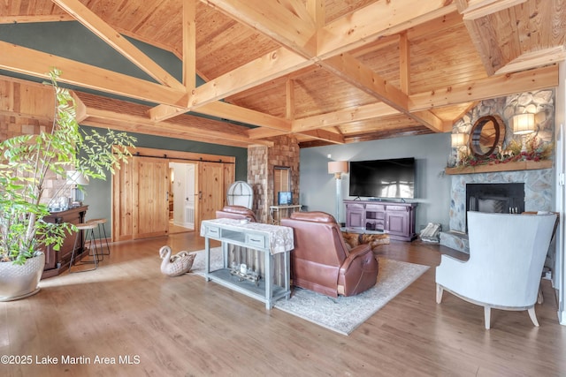 living room featuring a stone fireplace, wood ceiling, lofted ceiling with beams, hardwood / wood-style flooring, and a barn door