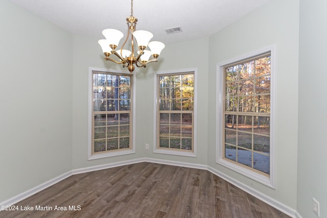 unfurnished dining area with dark wood-type flooring, a textured ceiling, and a notable chandelier